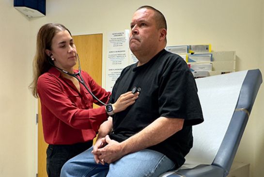 A doctor listens to her patient's heartbeat with a stethoscope during a checkup in a medical exam room.
